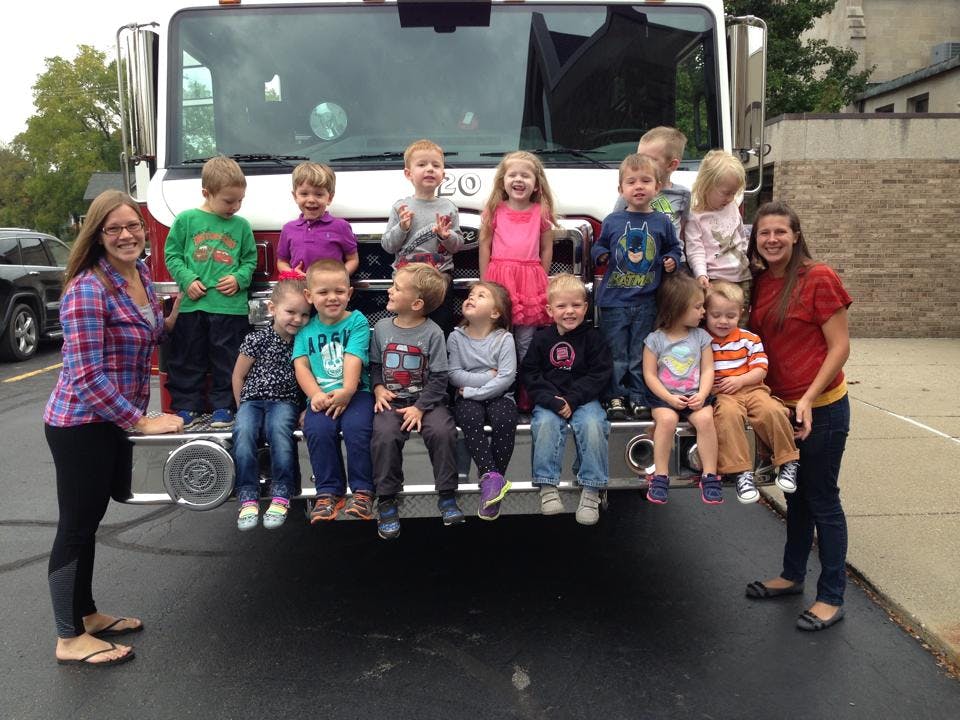 Two people and multiple children sitting on the front of a fire truck
