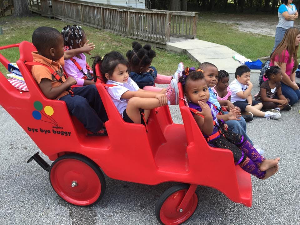 Children sitting in a red multi-seat stroller and on the ground