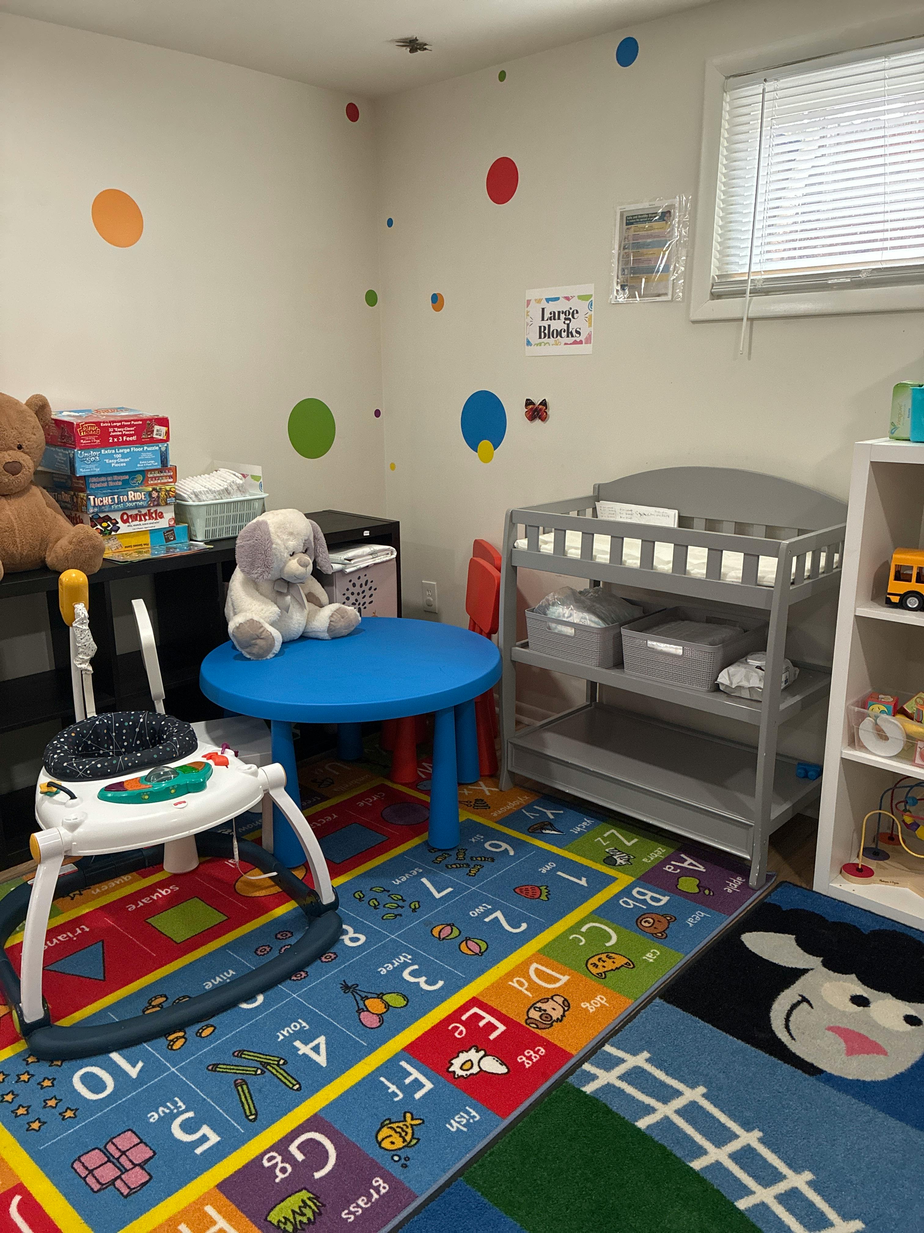 Child's room with an ABC rug, a blue table, a toy bassinet, and various toys