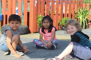 Three children sitting on the ground outdoors