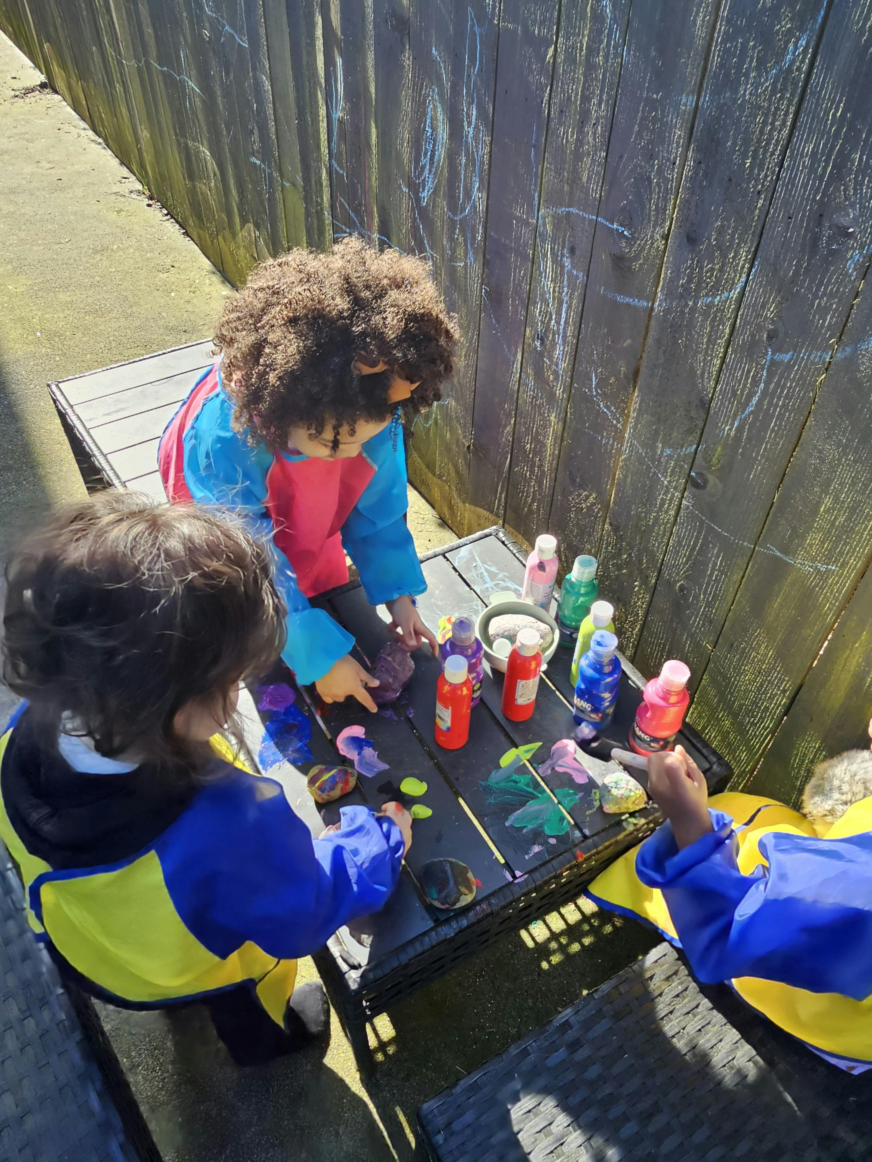 Children painting at a table outdoors