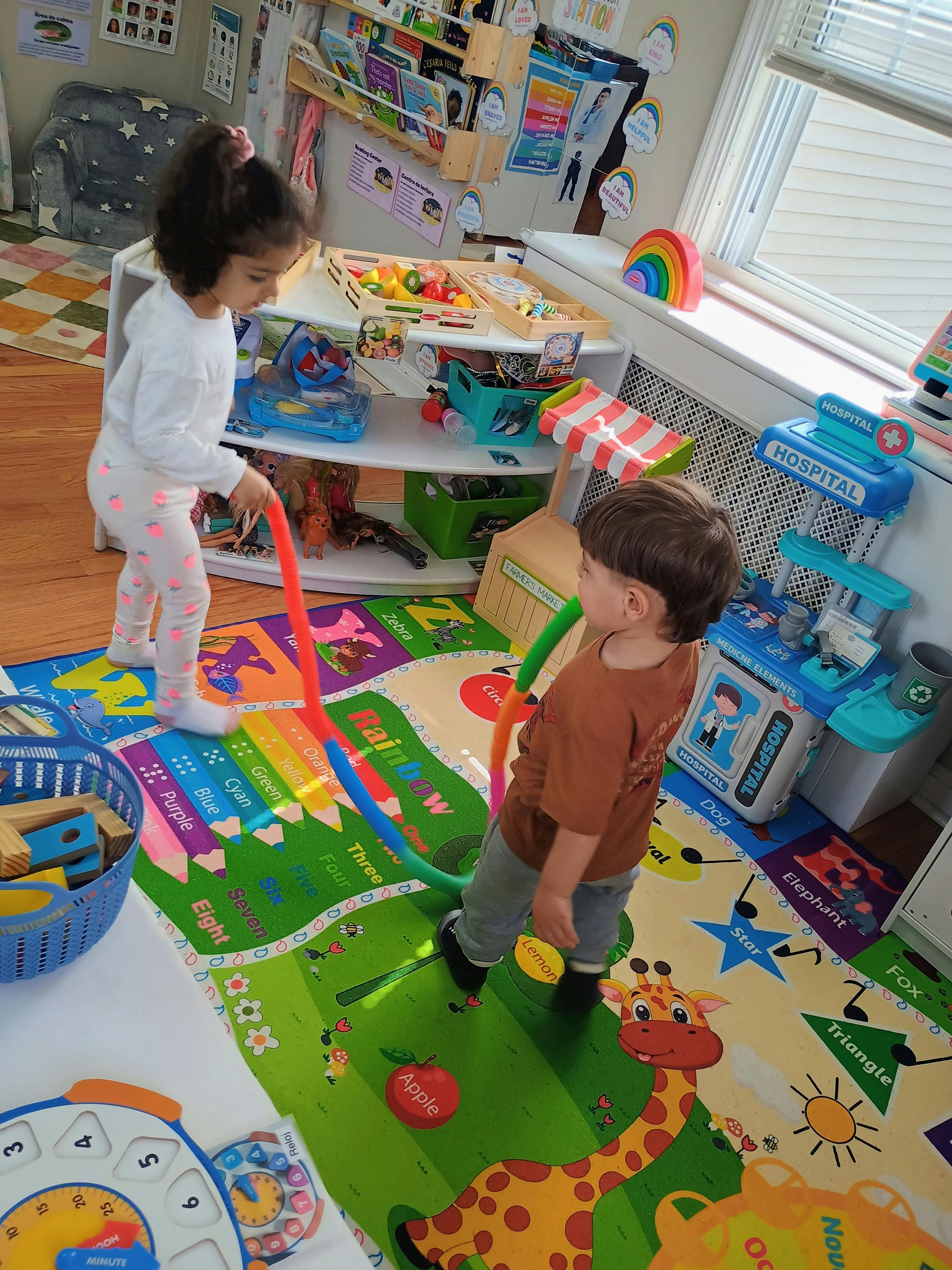 Two children playing with colorful pool noodles on a patterned playroom rug
