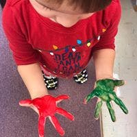 Child with hands covered in red and green paint