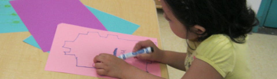 Child drawing on pink paper with a marker