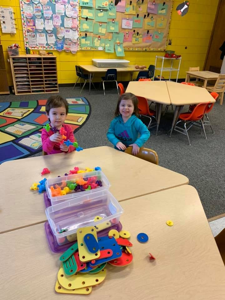 Two children playing with colorful building toys at a table in a classroom