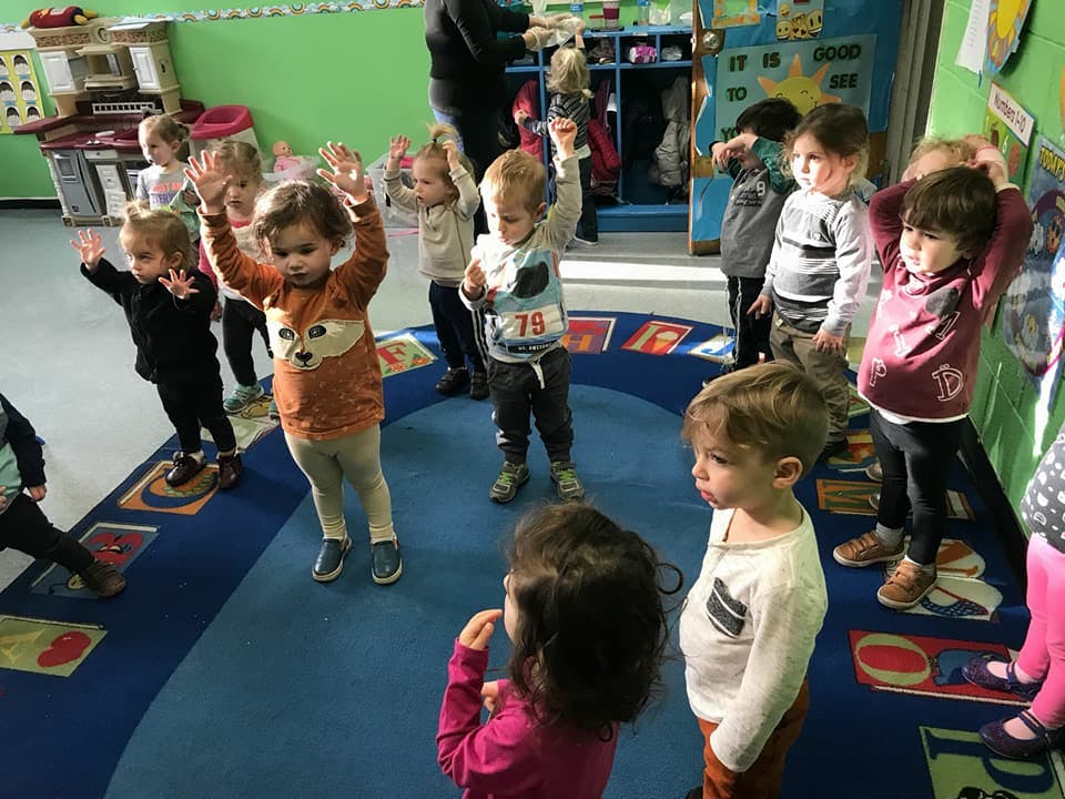 Children standing in a circle with their hands raised in a classroom