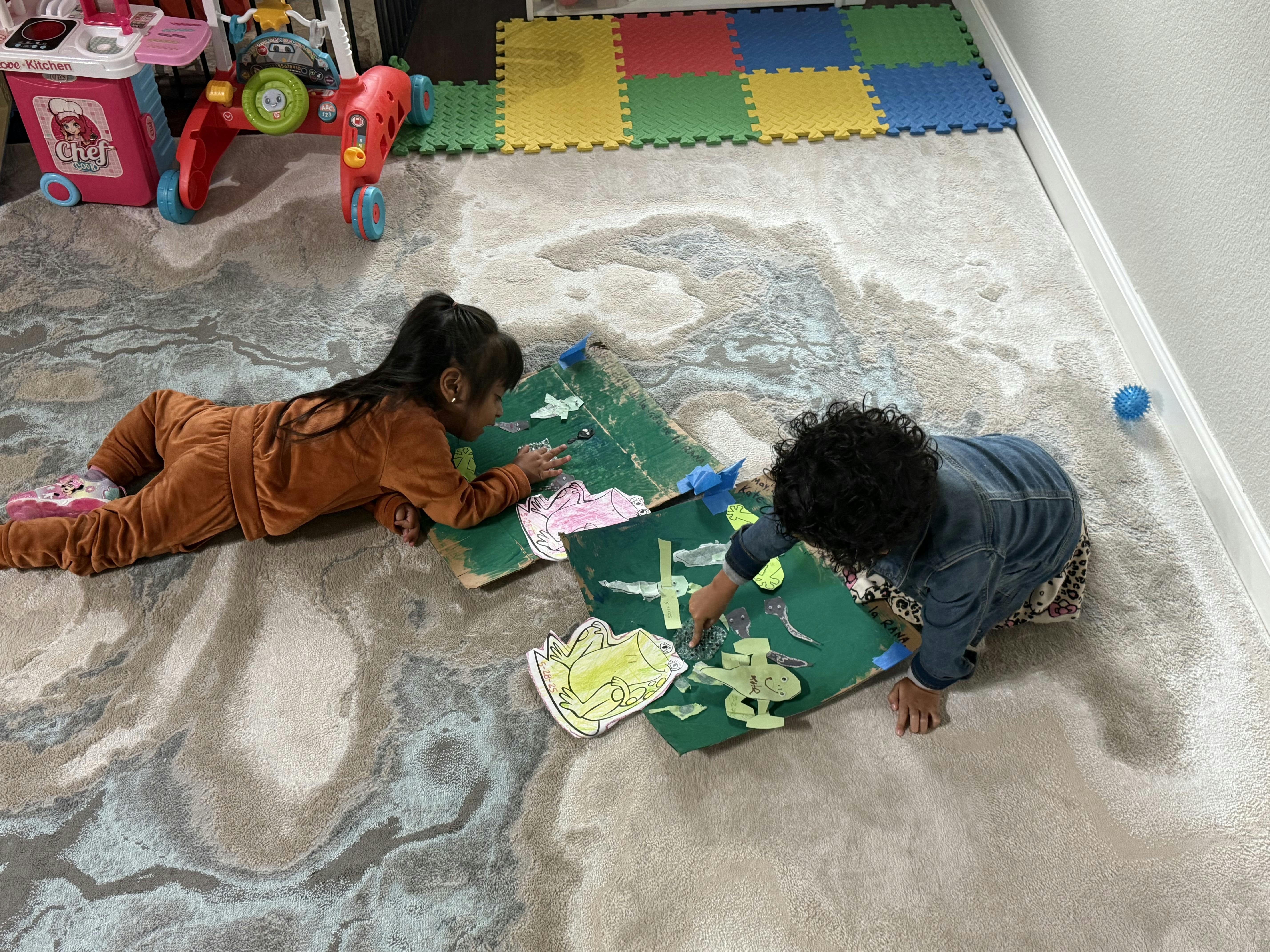 Two children playing with green craft boards on the floor