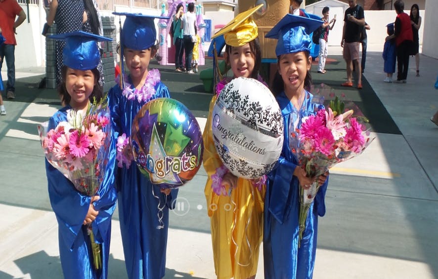 Four children in graduation caps and gowns holding flowers and balloons