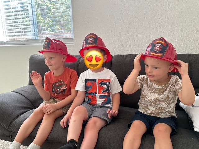 Three children wearing red firefighter hats sitting on a couch