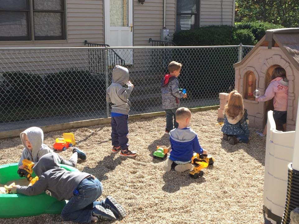 Children playing in a sandbox with toys and a playhouse