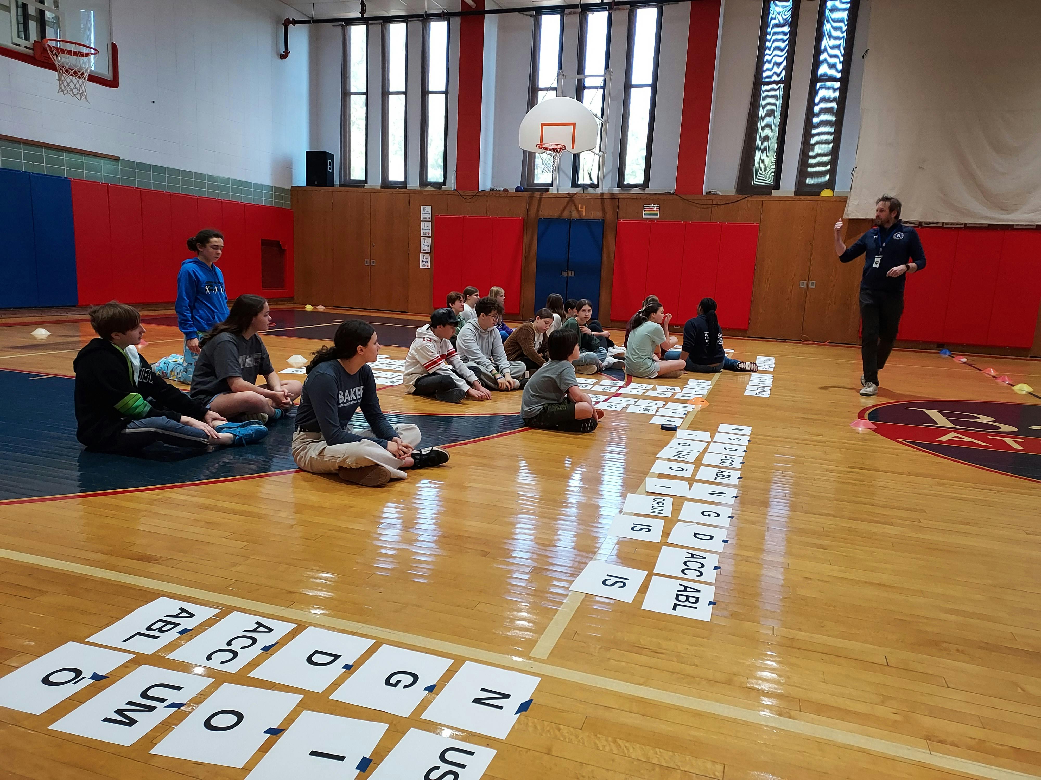 People sitting on a gym floor with cards laid out, one person standing