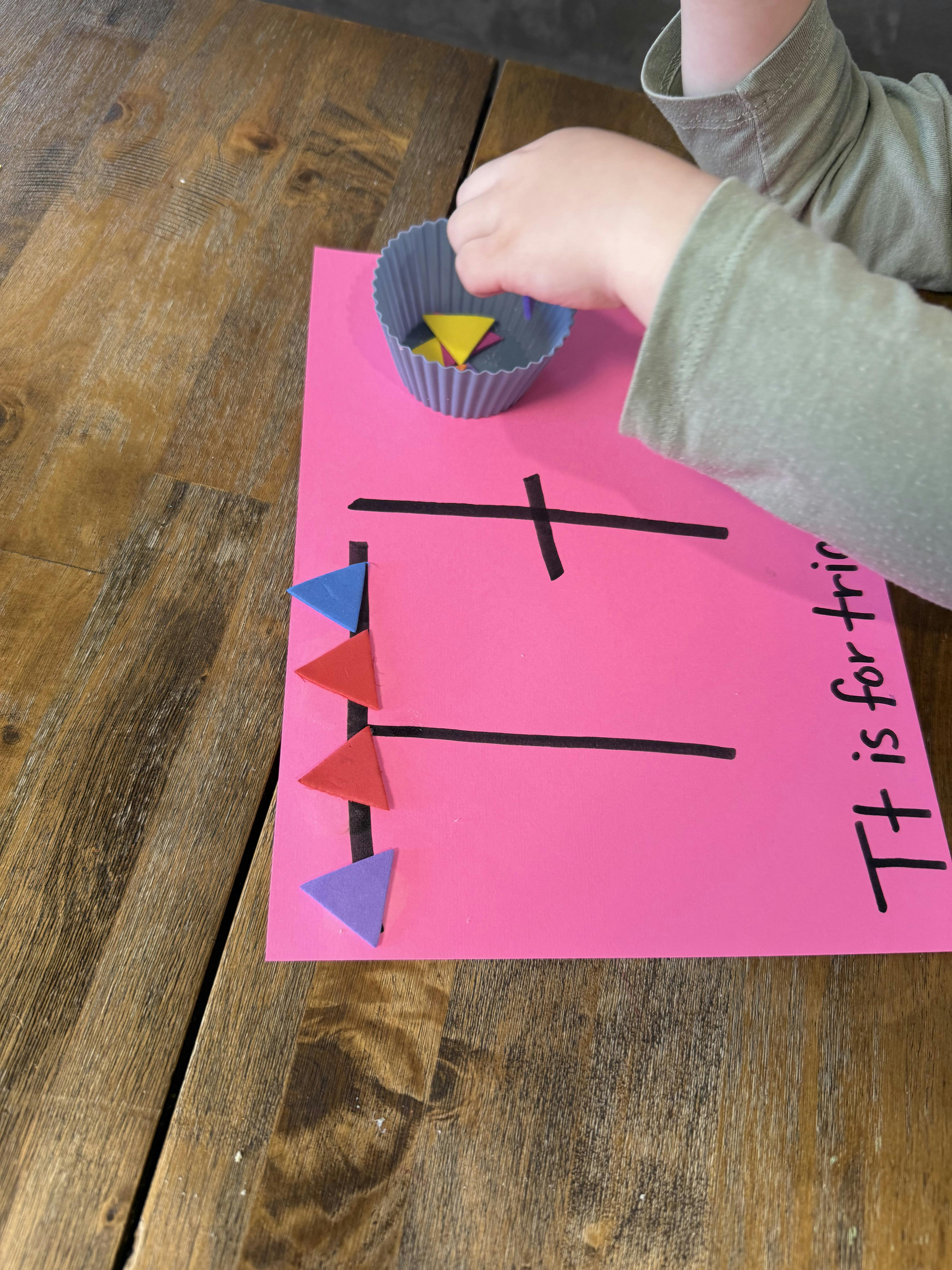Child's hands playing with triangle-shaped foam pieces on a pink paper