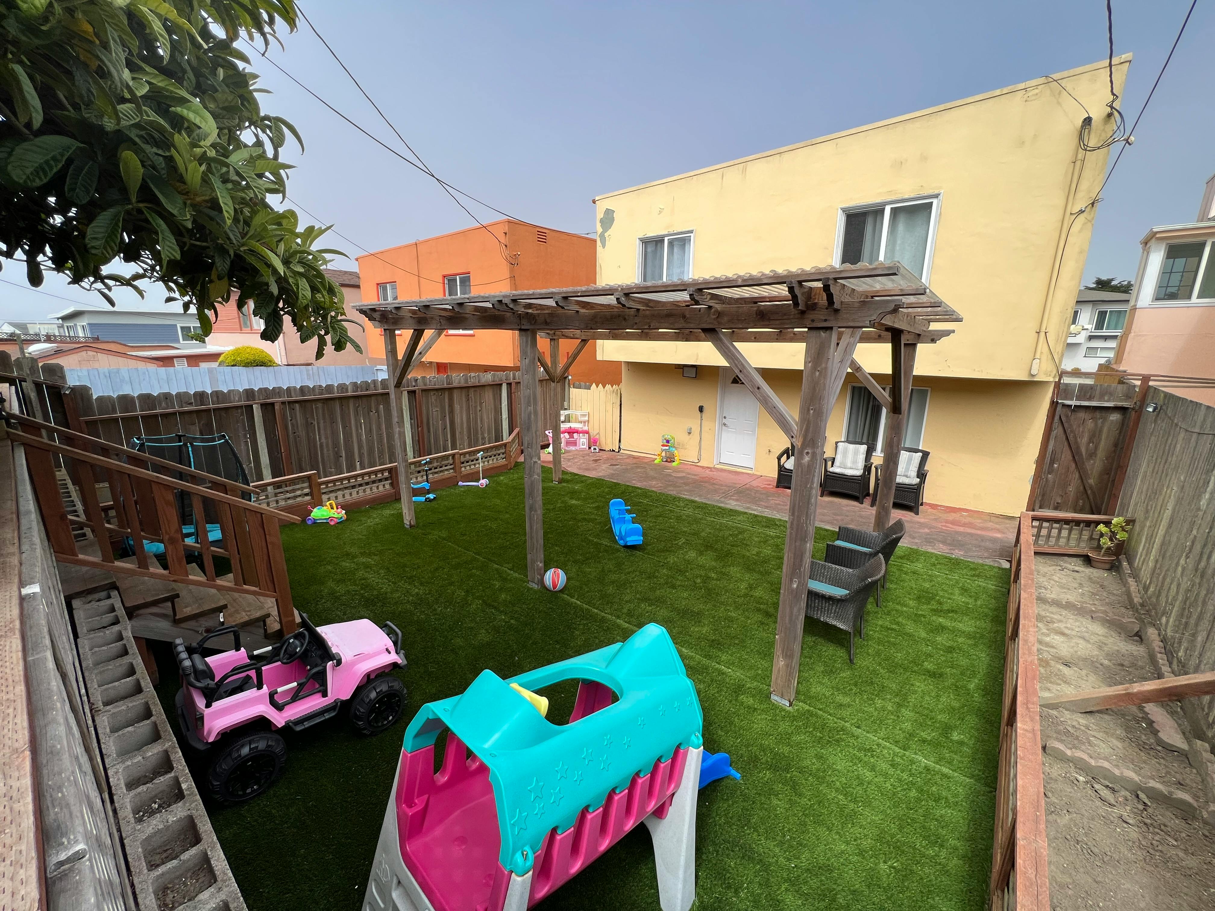Backyard with artificial turf, play structures, and a wooden pergola