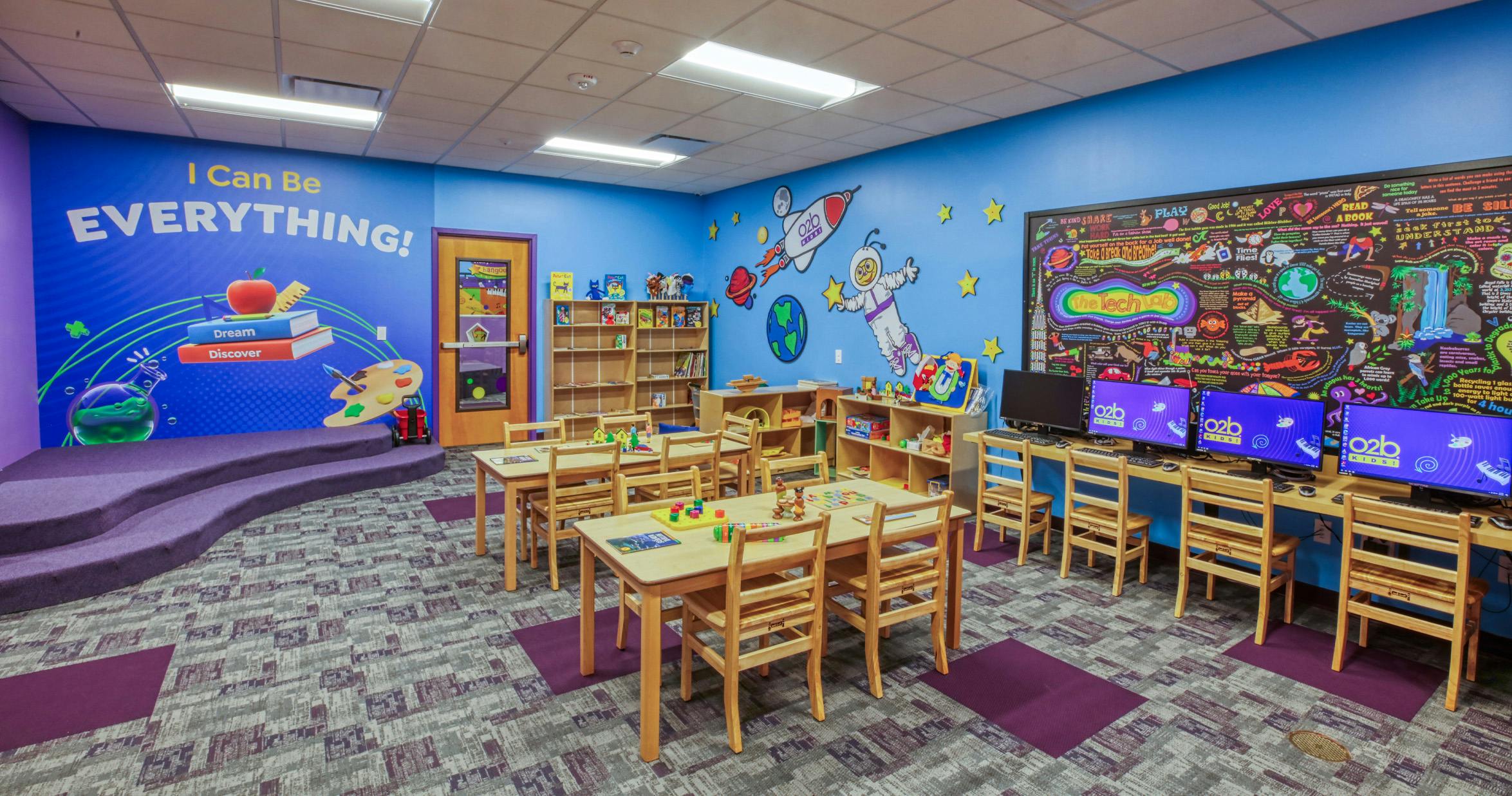 Children's classroom with brightly painted blue walls, small wooden tables, and computers