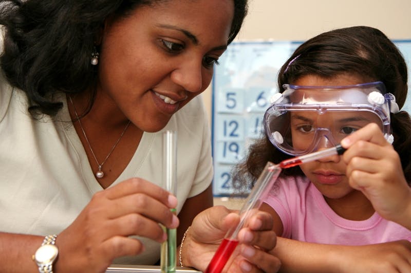 Person and child in safety goggles doing a science experiment with test tubes