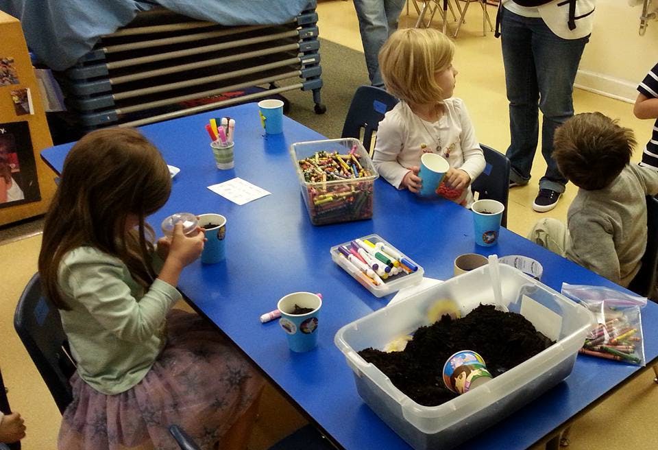 Children at a blue table with craft supplies and a bin of soil