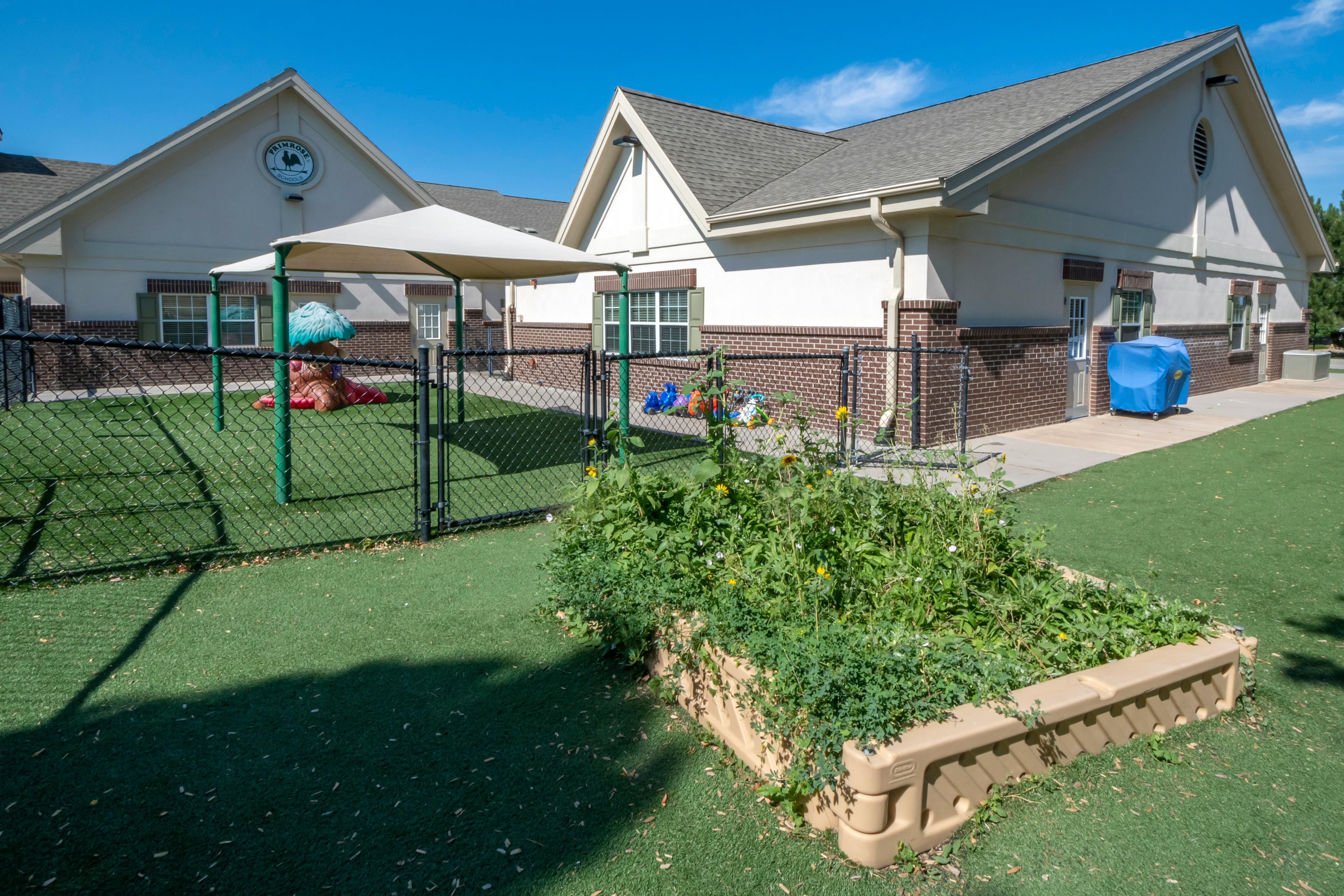 A beige building with a playground and raised garden bed on artificial turf