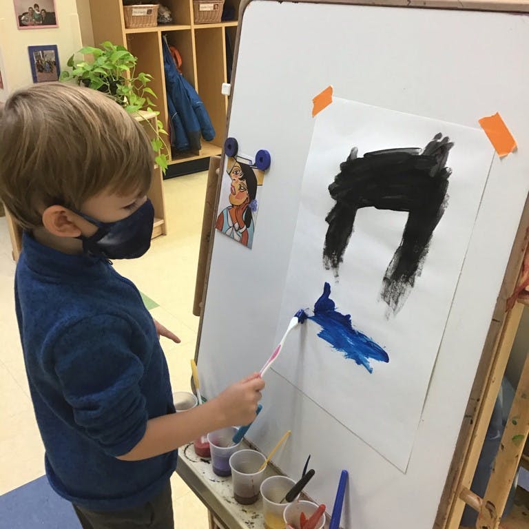 Child in a mask painting on an easel