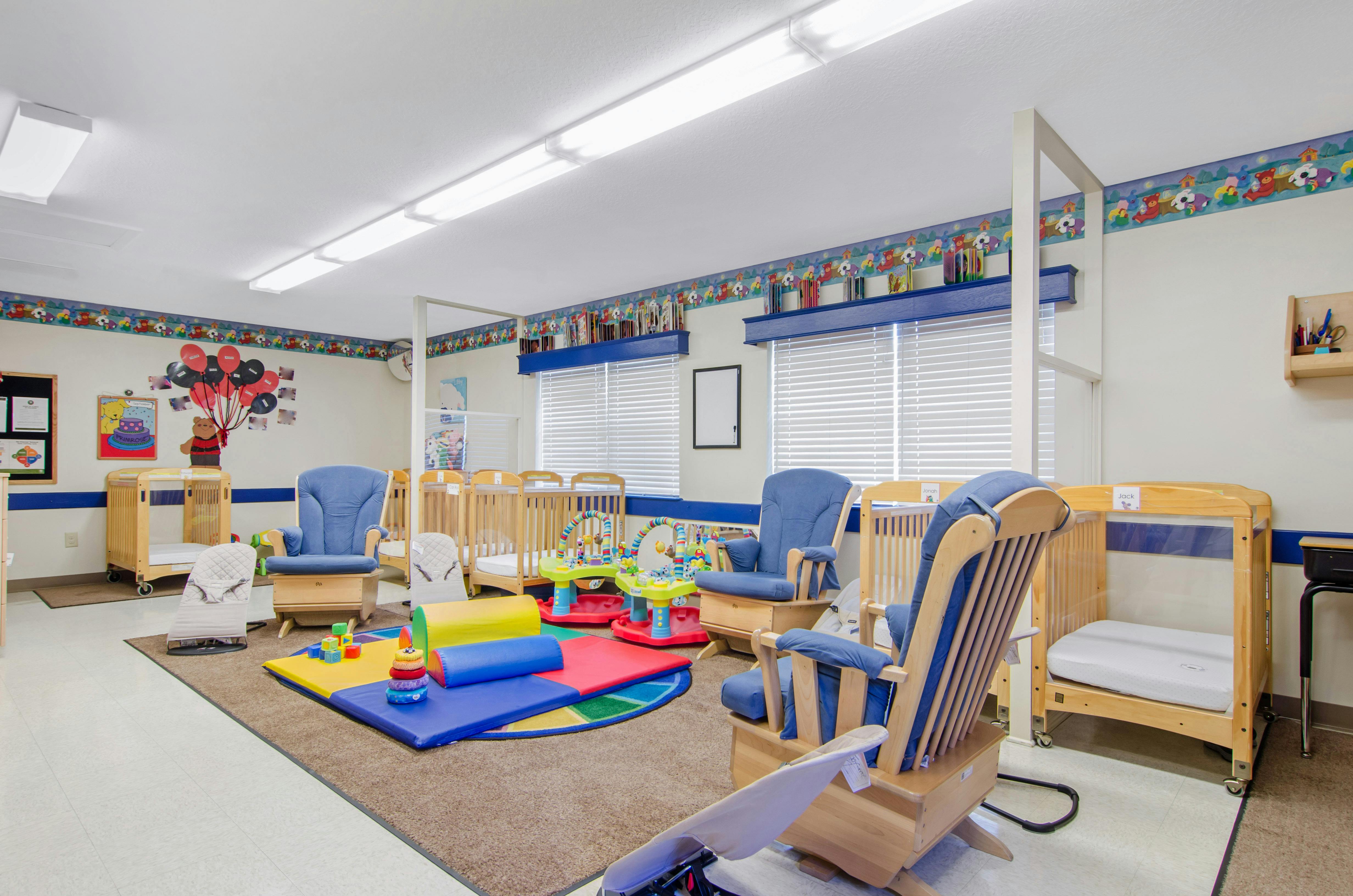 An empty nursery room with cribs, rocking chairs, and play mats