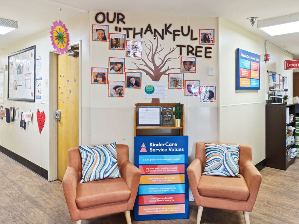 Lounge area with two chairs facing a KinderCare service values sign and thankful tree display