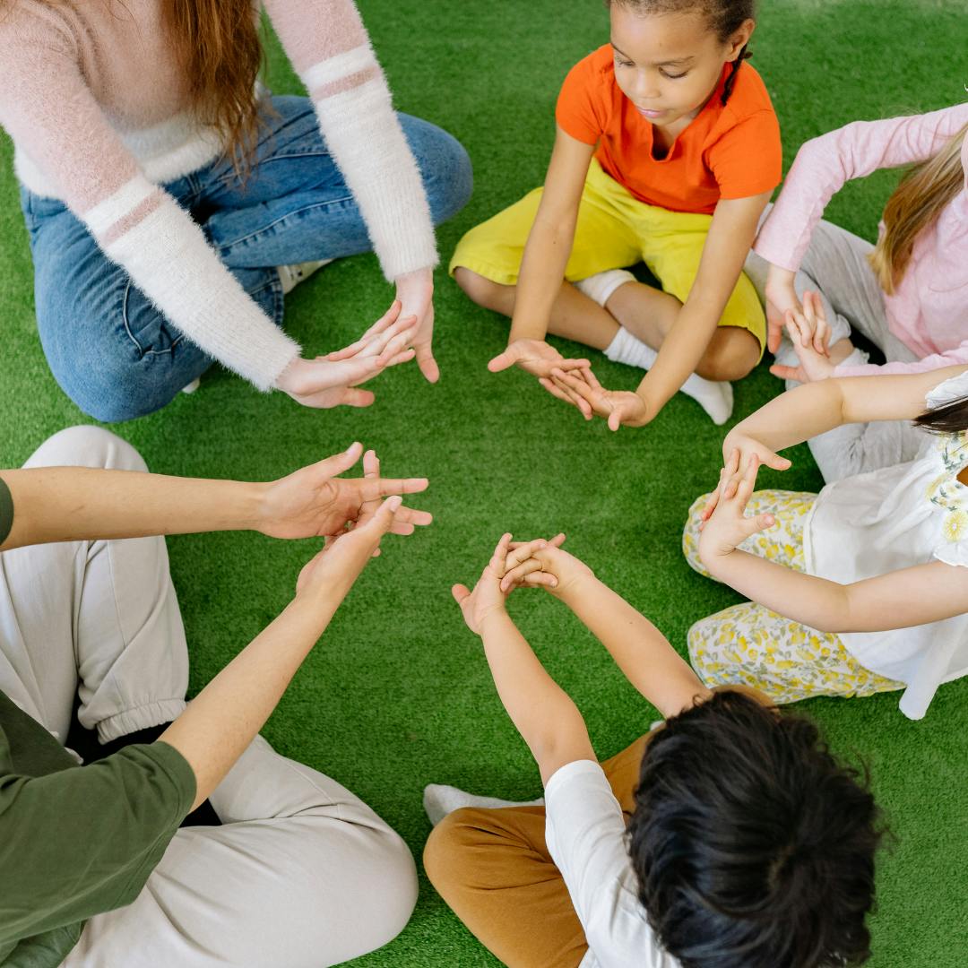 People and children sitting in a circle with hands in the middle