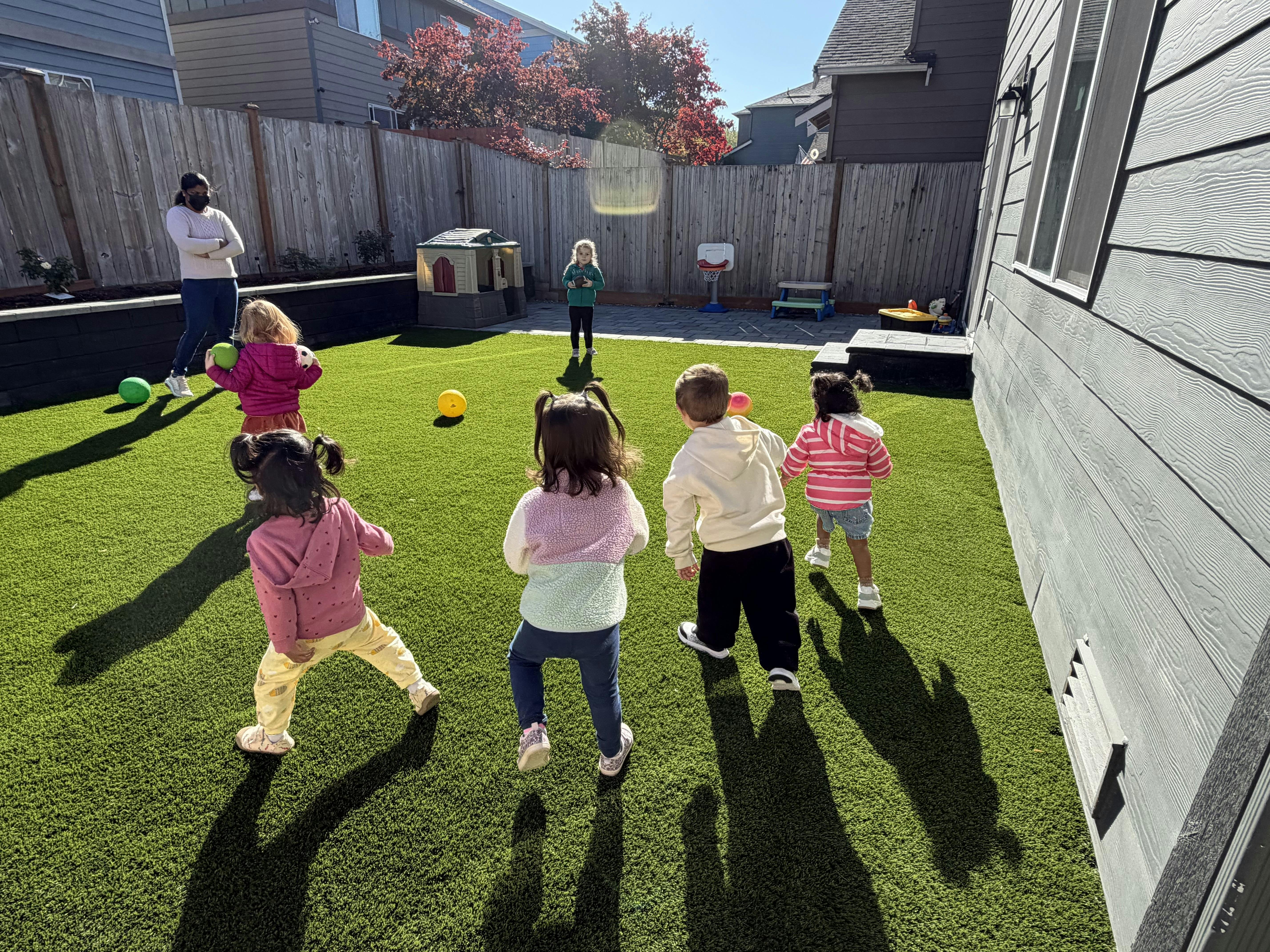 A person and multiple children playing in a fenced backyard