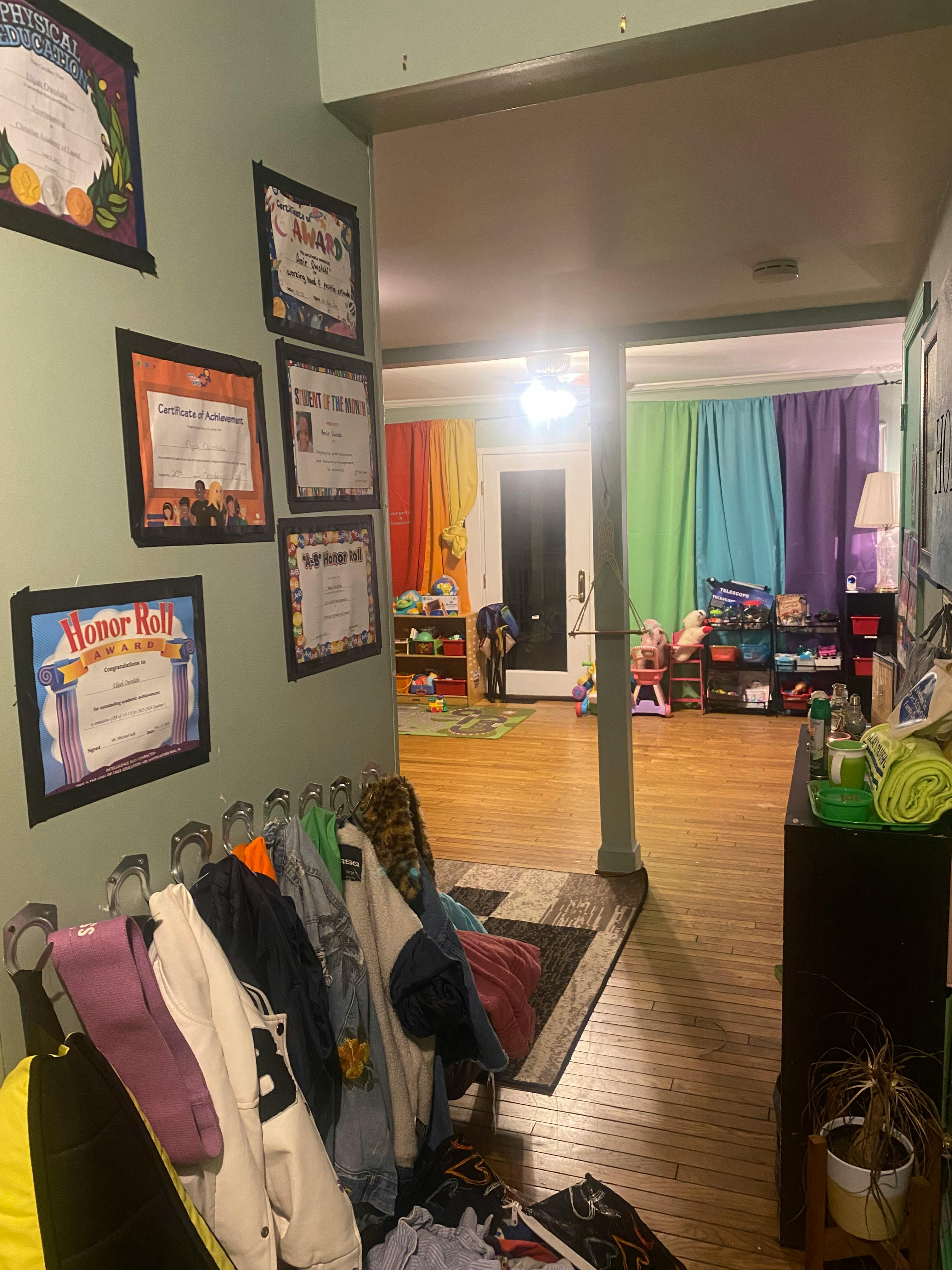Hallway with framed certificates on wall and clothes on a rack, leading to a room with colorful curtains