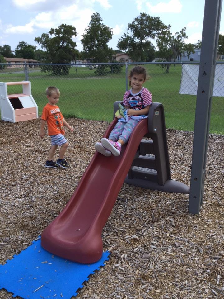 Child sitting on a slide with another child standing nearby on a playground