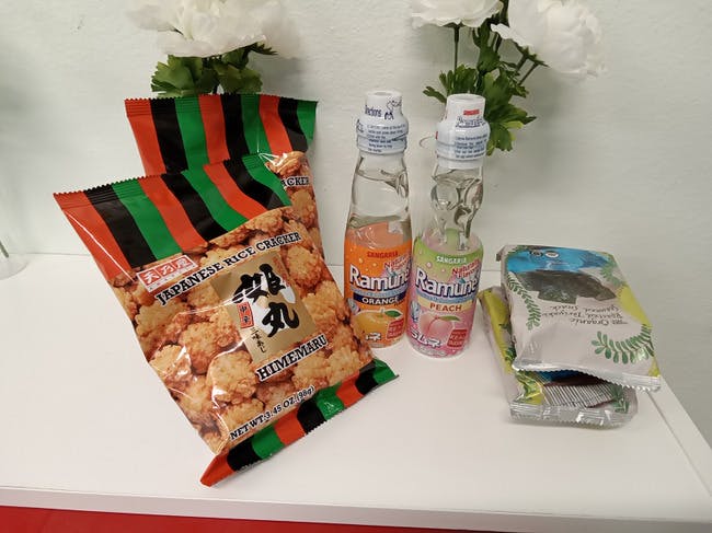Bags of Japanese rice crackers, two bottles of Ramune, and seaweed snacks