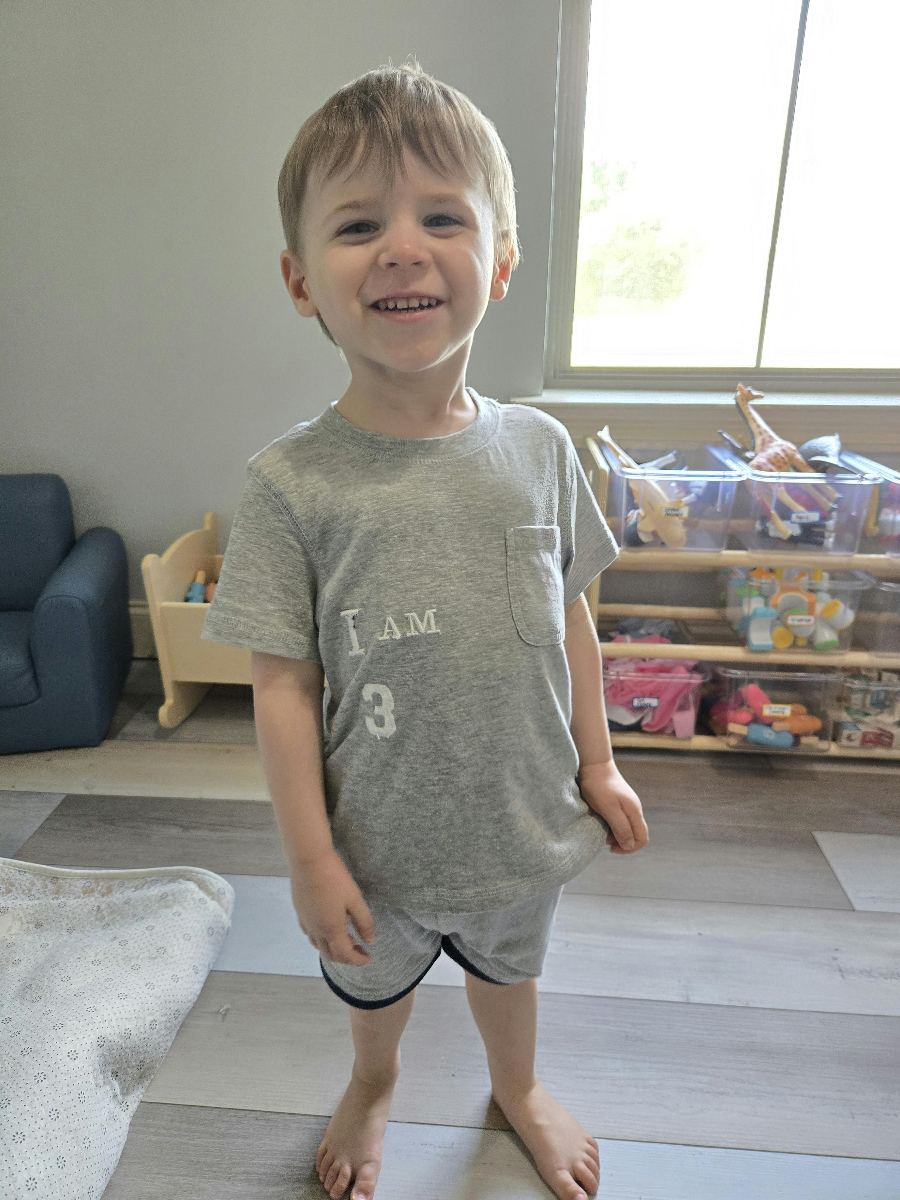 Child wearing a gray shirt with "I AM 3" printed on it