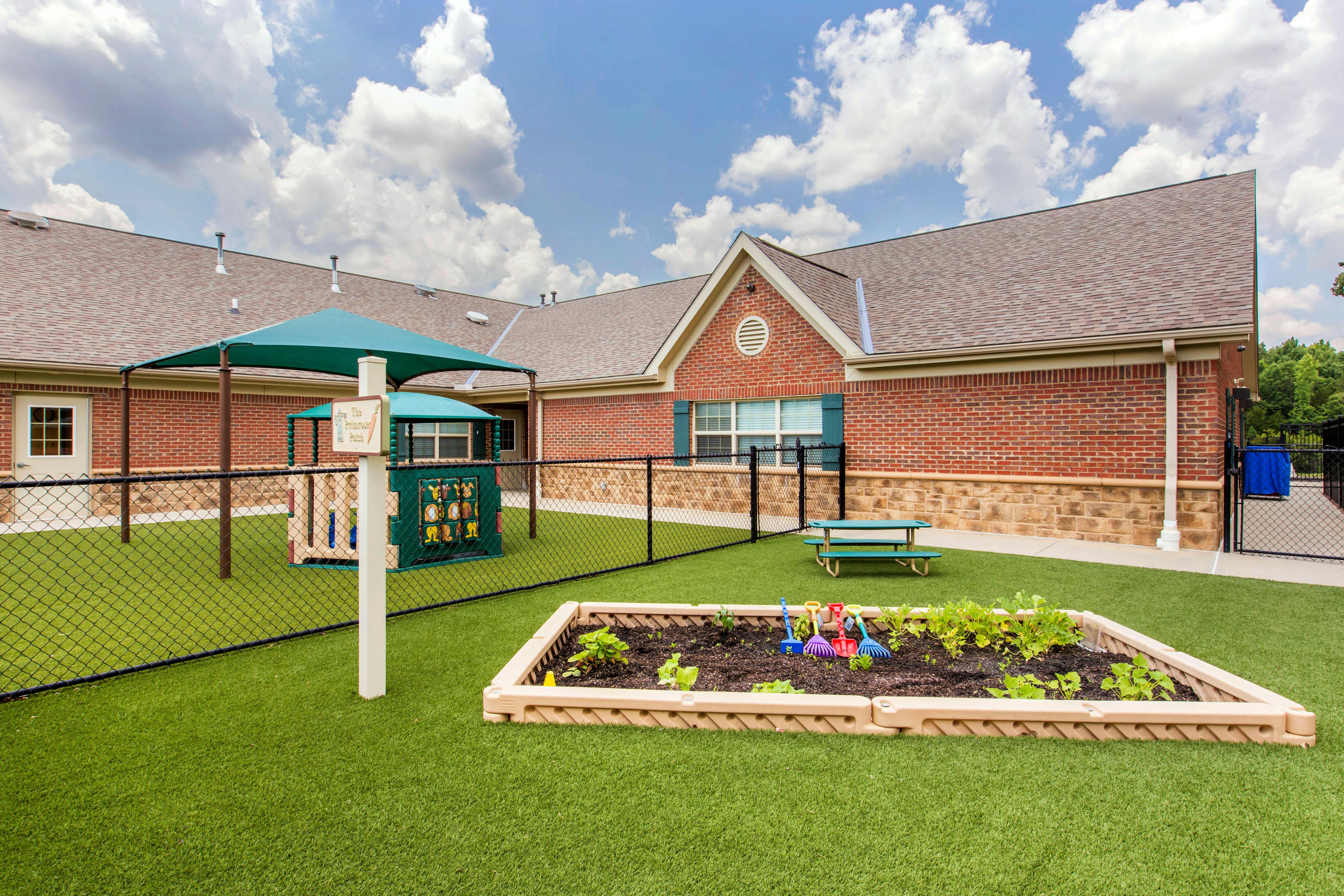 Fenced playground with artificial turf, a garden, play structure, and brick building