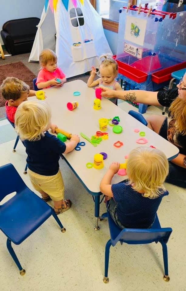 Children playing with modeling clay at a table in a classroom