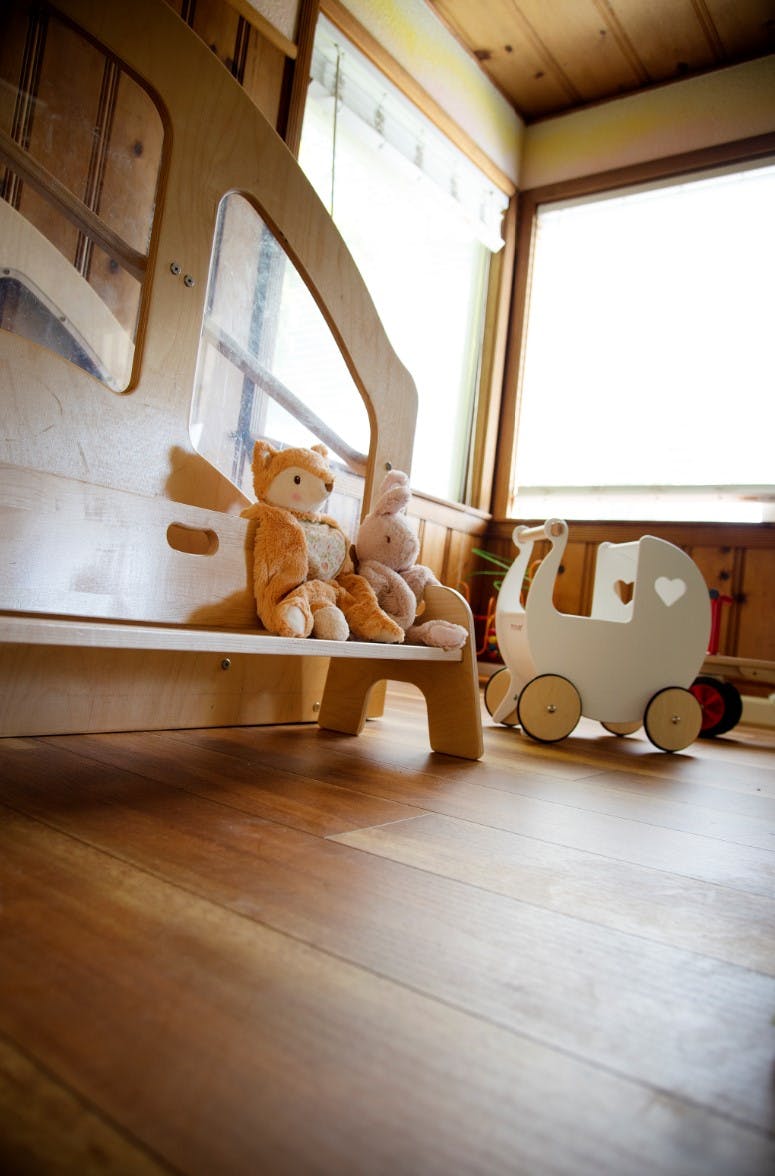 Stuffed fox and rabbit toys sitting on a wooden bench next to a toy pram