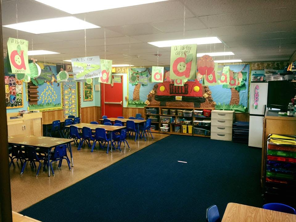 Classroom with small tables and chairs, blue carpet, and decorated walls