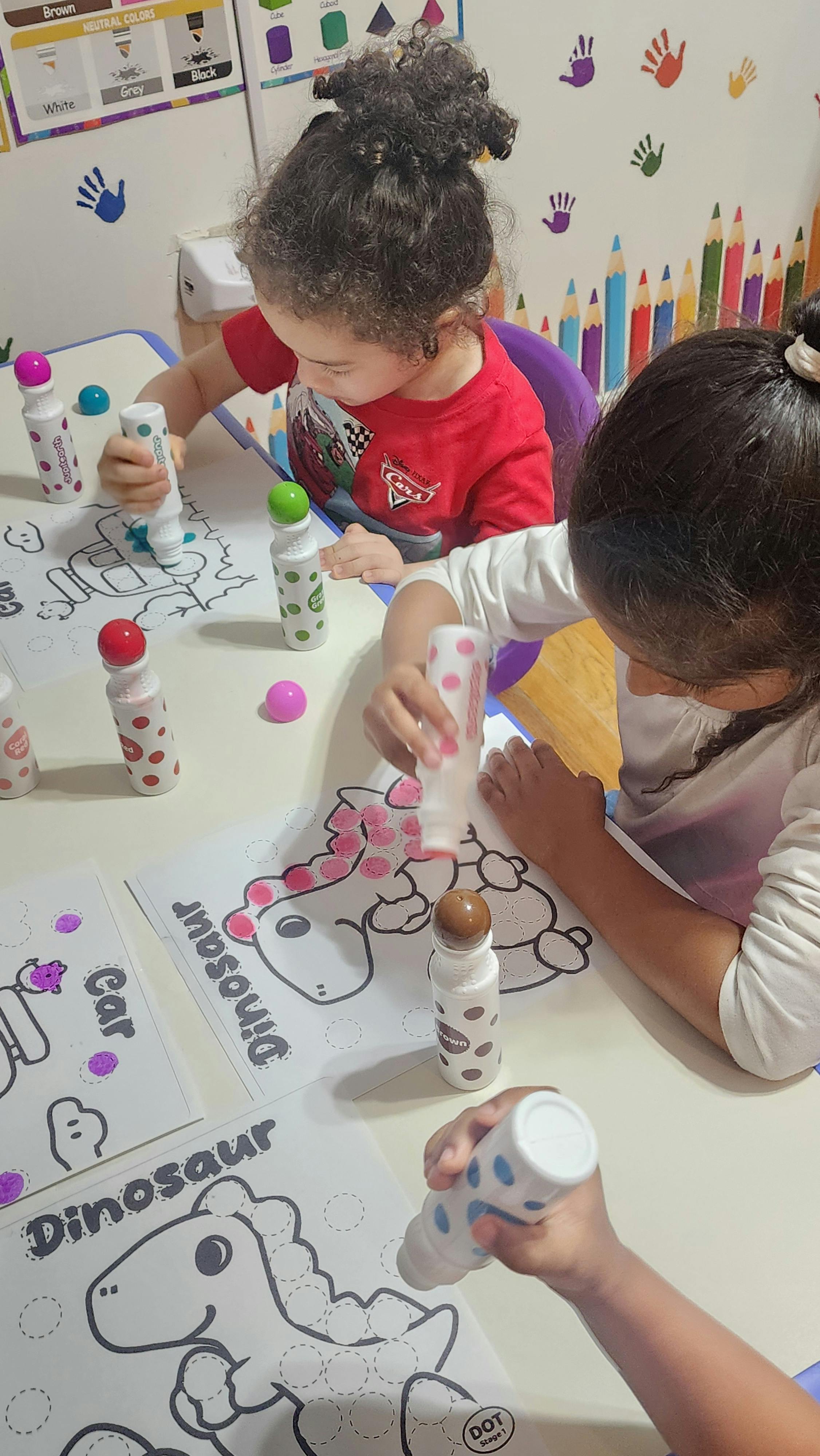 Children using dot markers to color in dinosaur and car worksheets