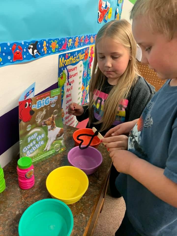 Two children making bubbles with wands and colorful bowls
