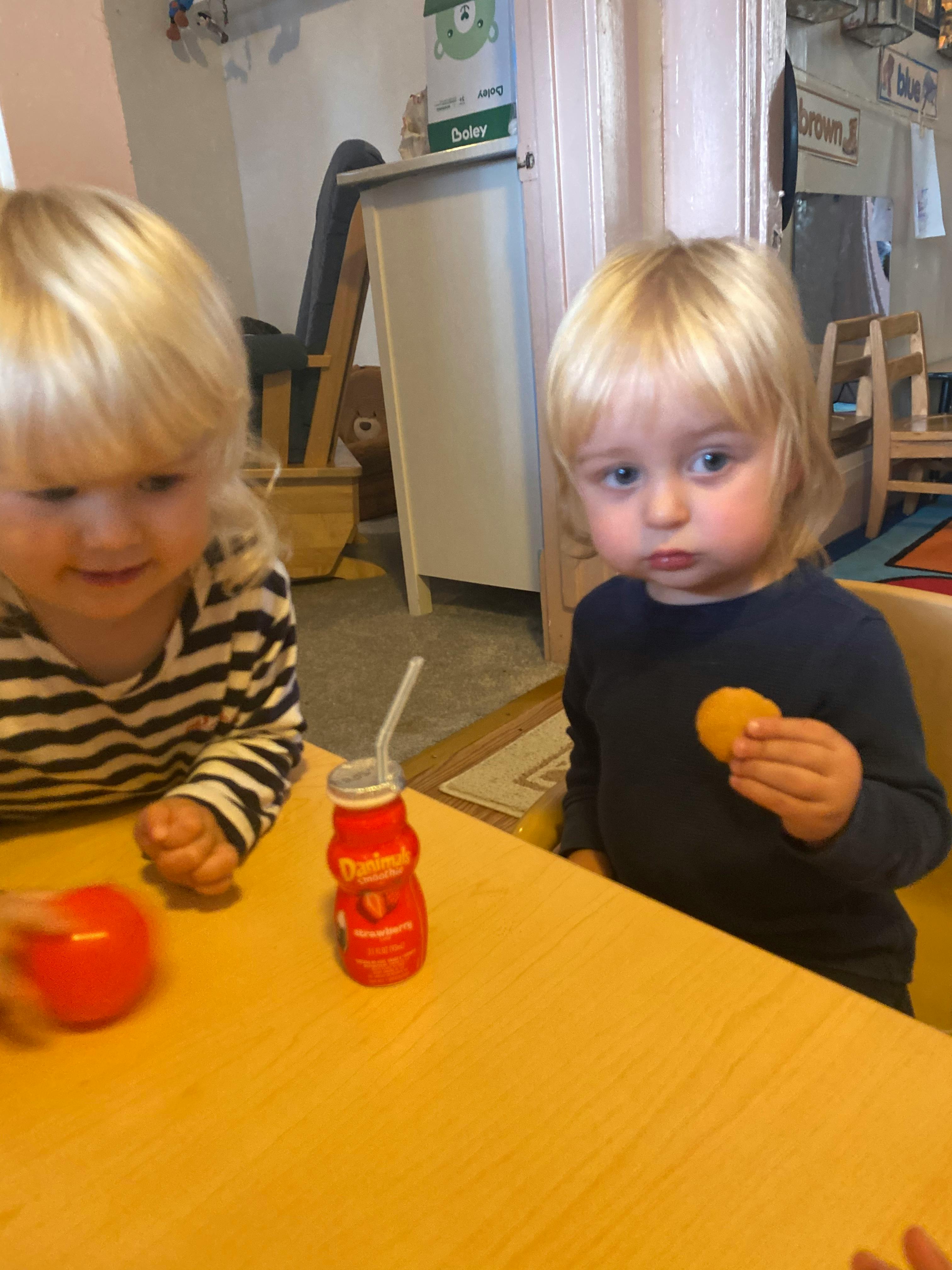 Two children at a table, one holding a cookie and the other with a drink
