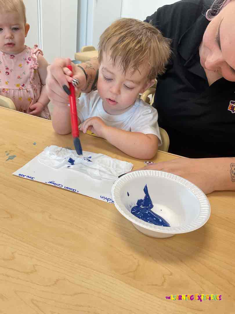 Adult helping a child paint with blue paint on crumpled paper