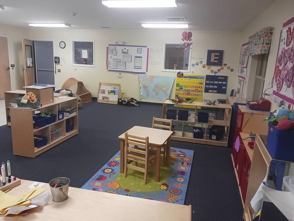 Classroom with small tables and chairs, shelves with toys, and wall decorations