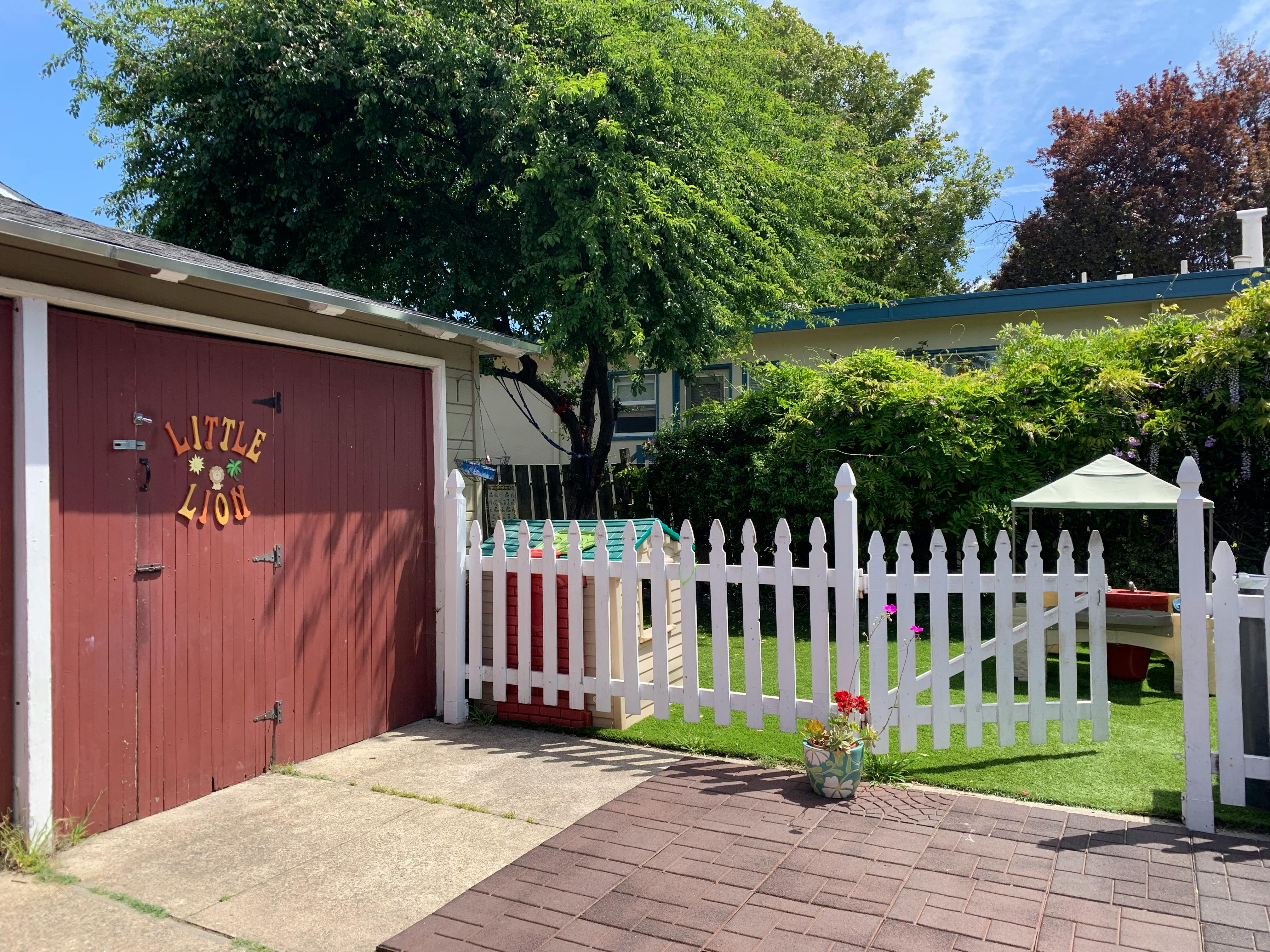 Red garage door with a white picket fence and green lawn