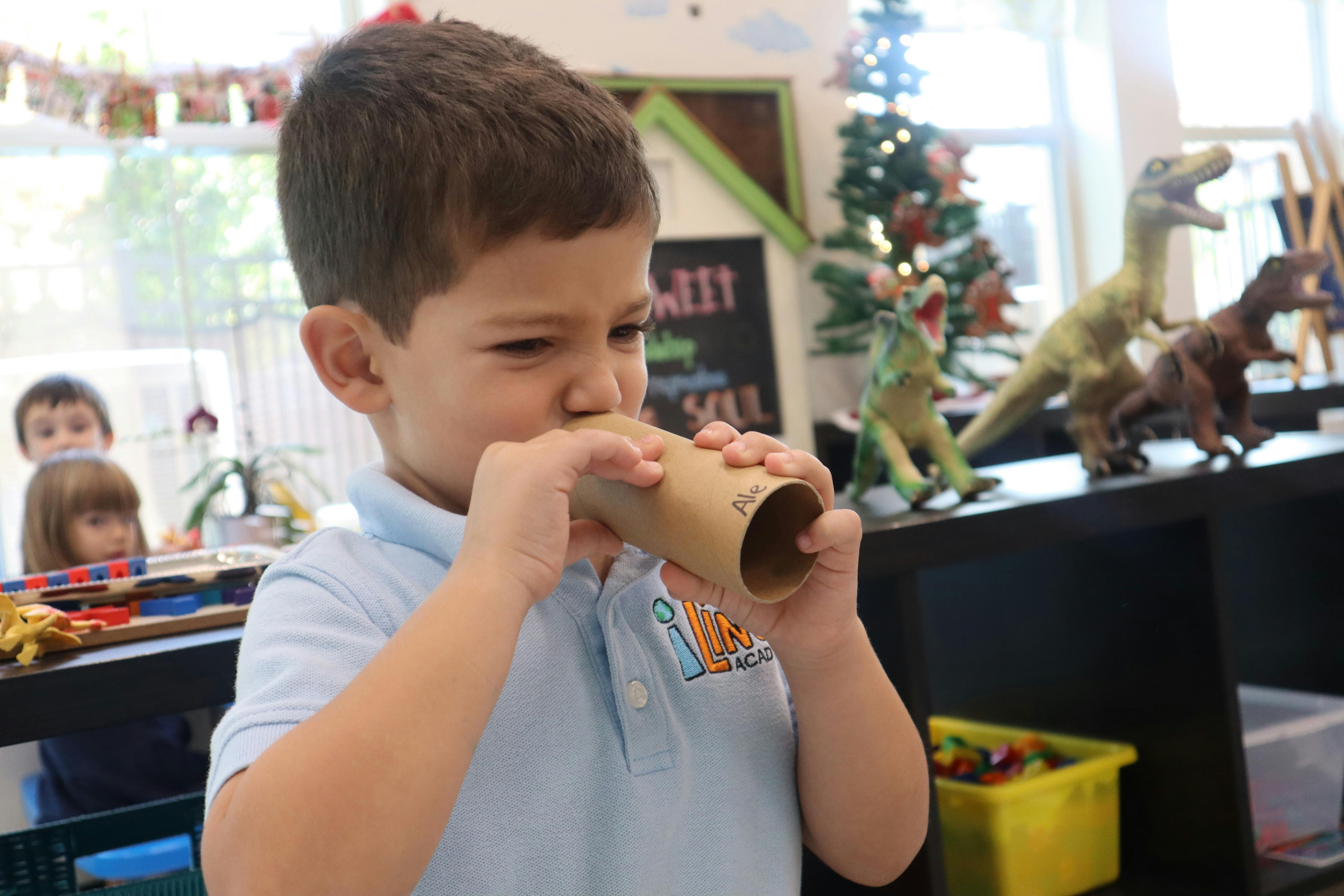 Child holding a cardboard tube to their mouth in a classroom