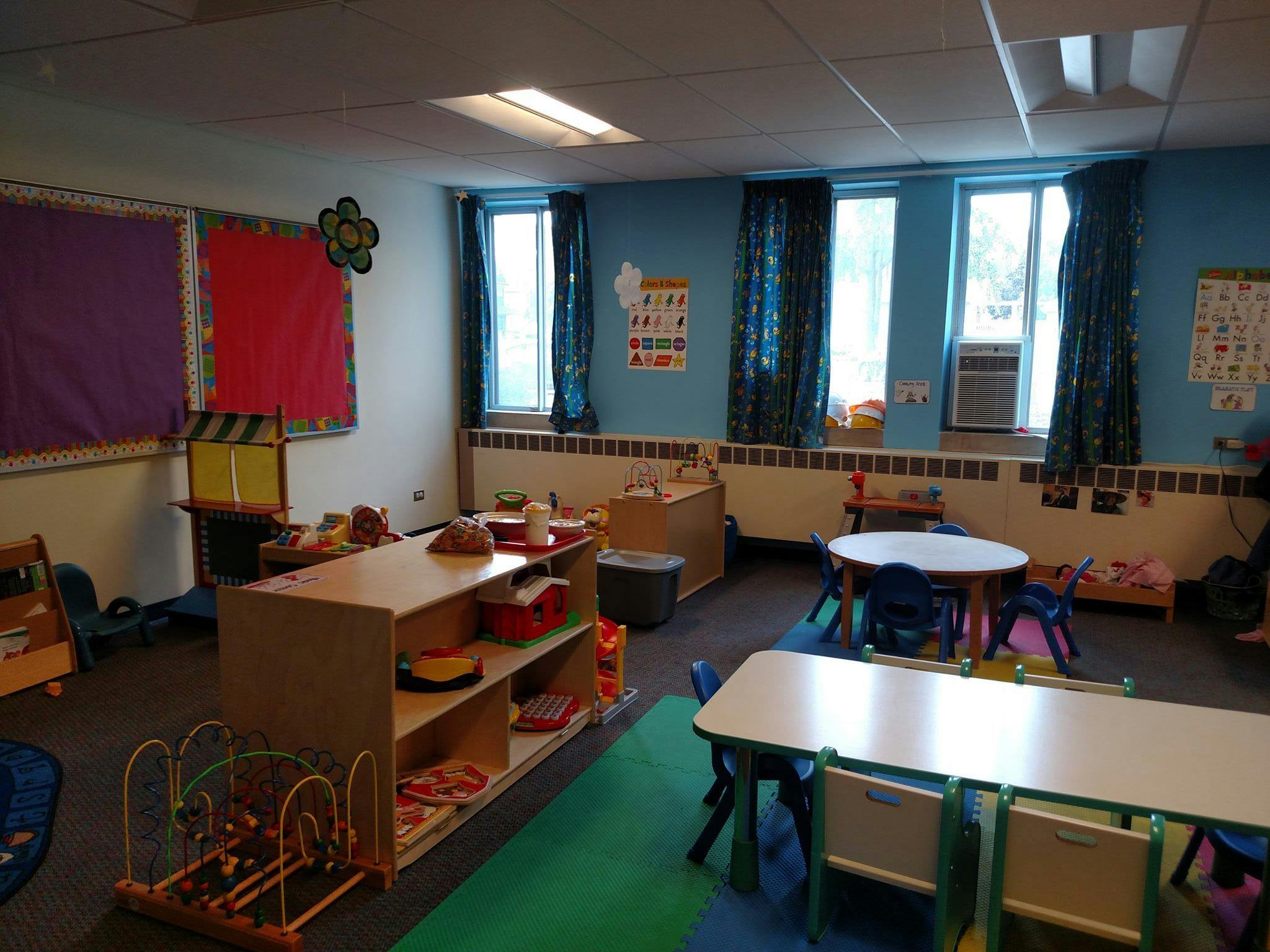 Classroom with small tables and chairs, shelves with toys, and windows