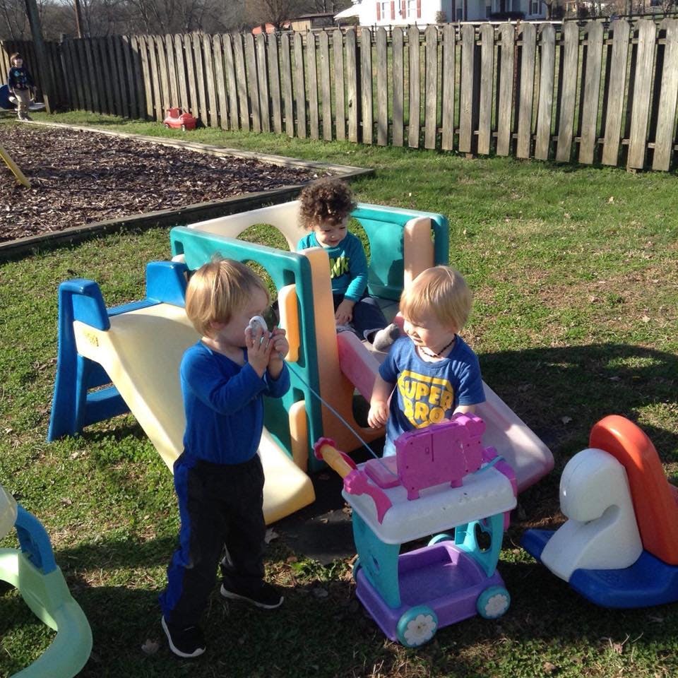 Three children playing on a small slide and with toys outdoors