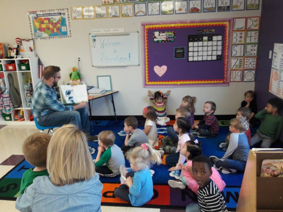 Adult reading a book to a group of children in a classroom
