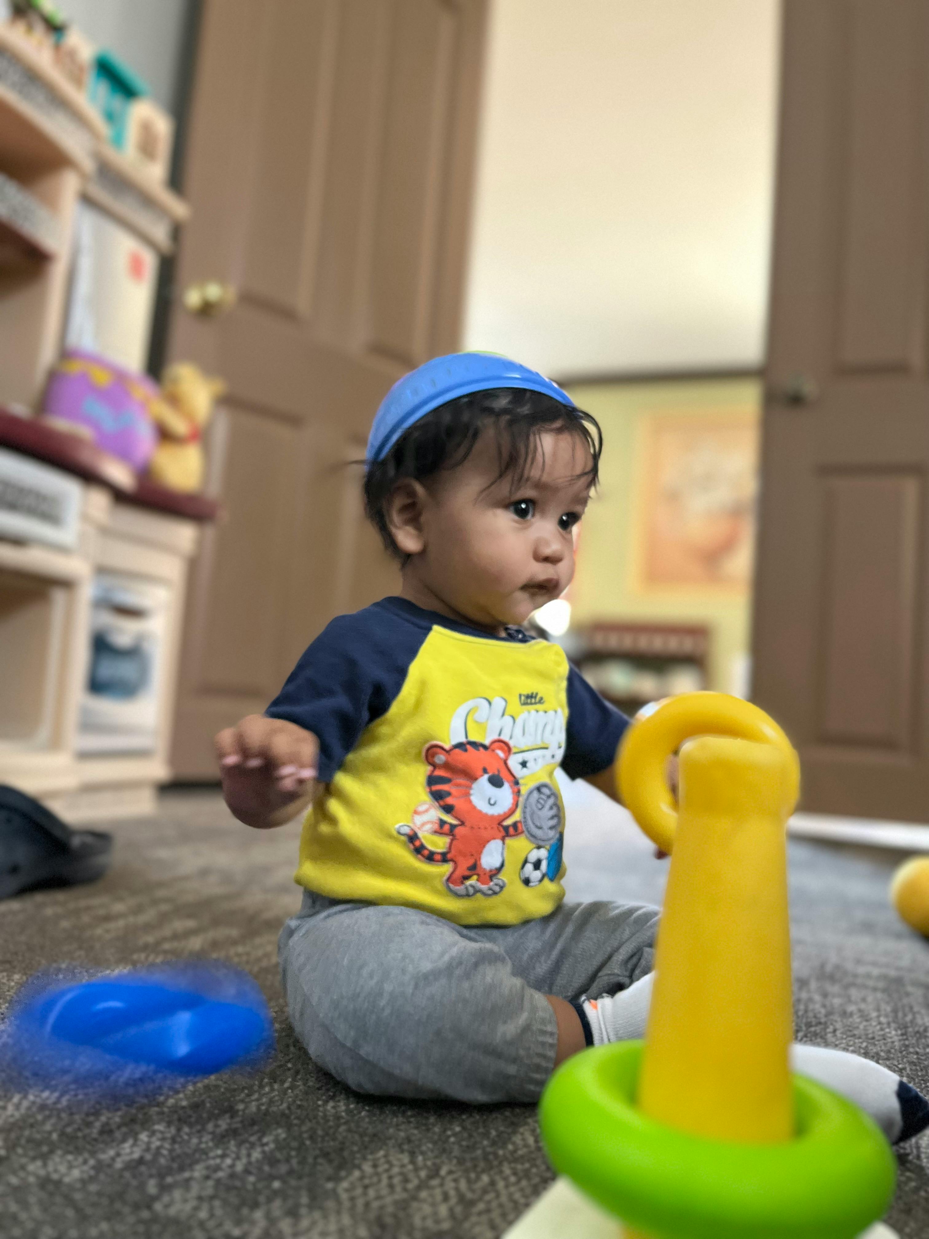 Child wearing a blue hat and yellow shirt sitting on the floor with toys