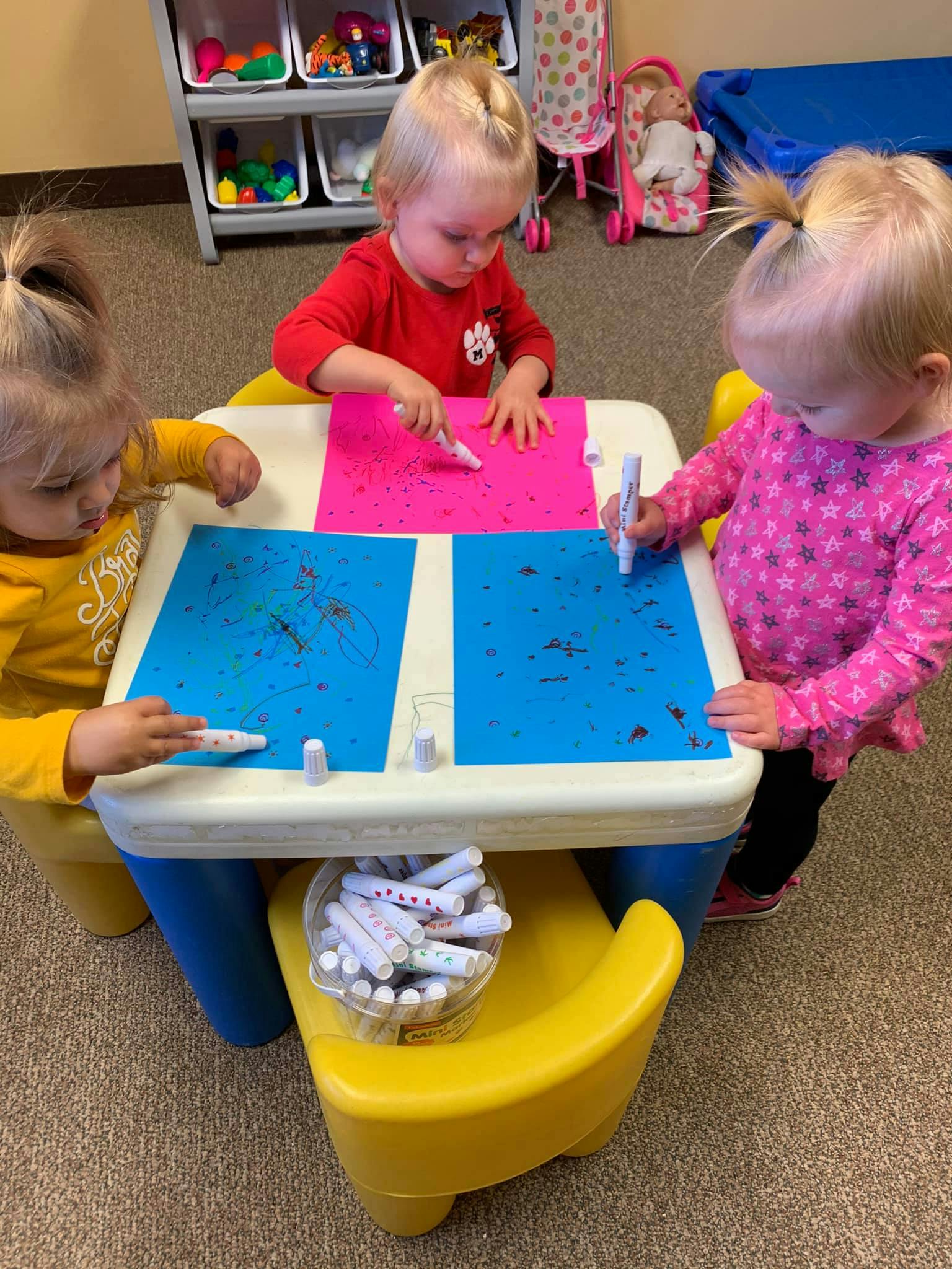 Three children drawing on paper at a small table
