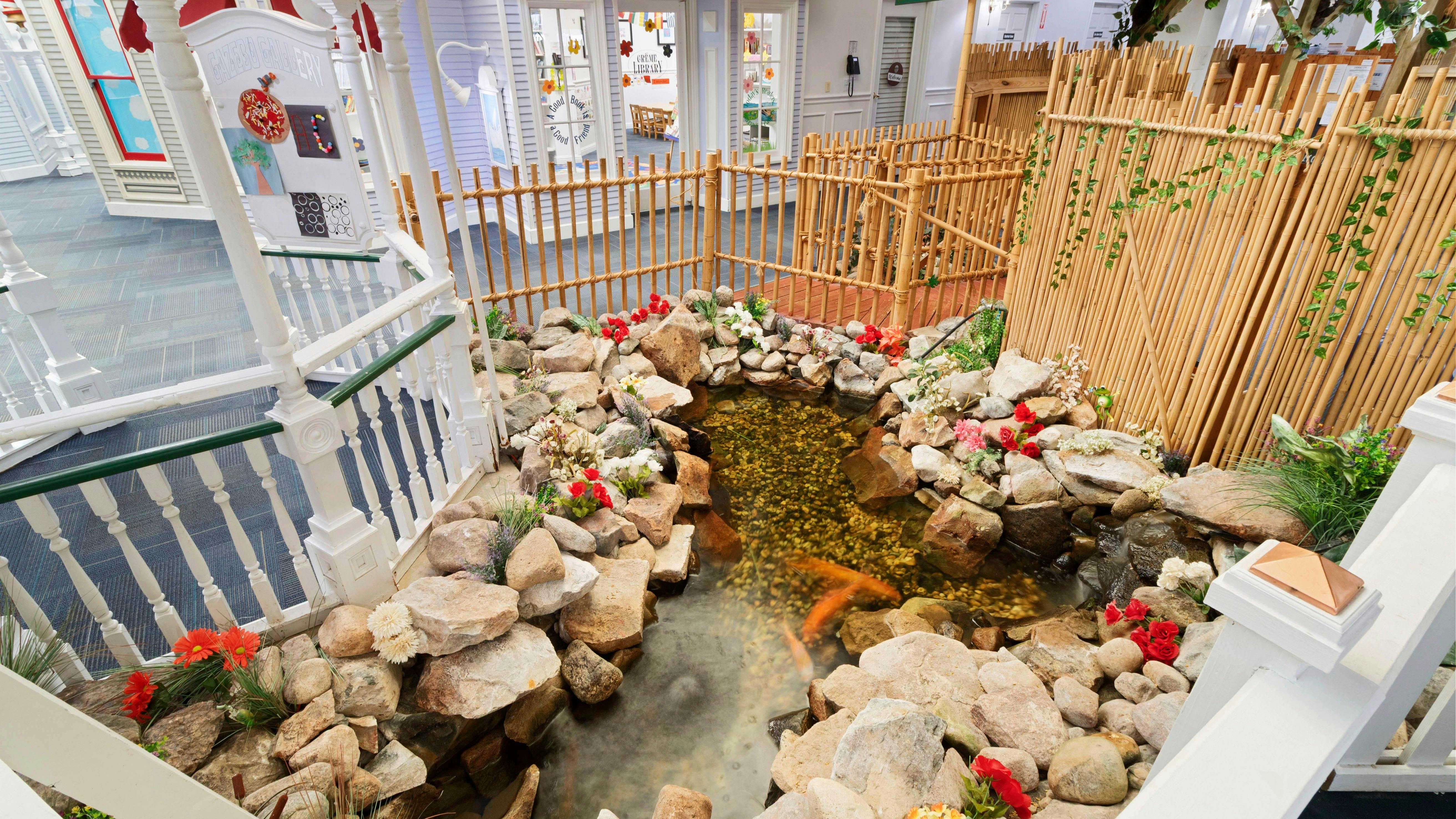 Curb view of a koi pond with red flowers and a bamboo fence in an indoor setting
