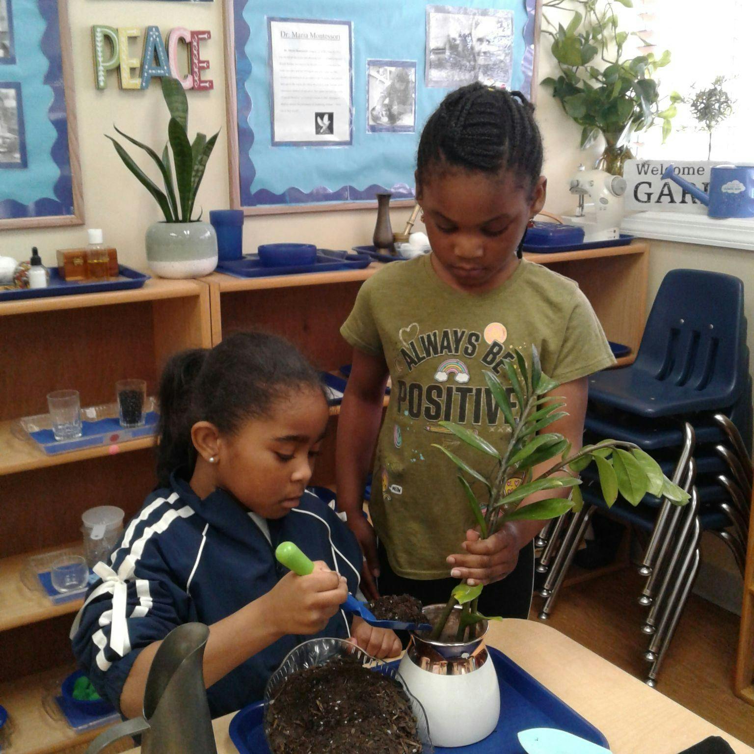Child planting in a pot while another child holds a plant