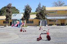 Tricycles on a paved area in front of a building and playground equipment