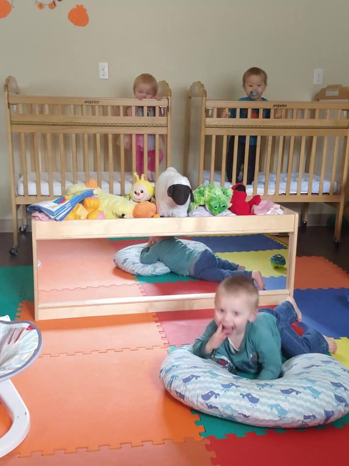 Three children in a room with two cribs and a mirror